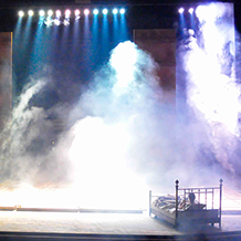 Beams of bright light shine down on Prior Walter while laying in bed as the wall falls around him.