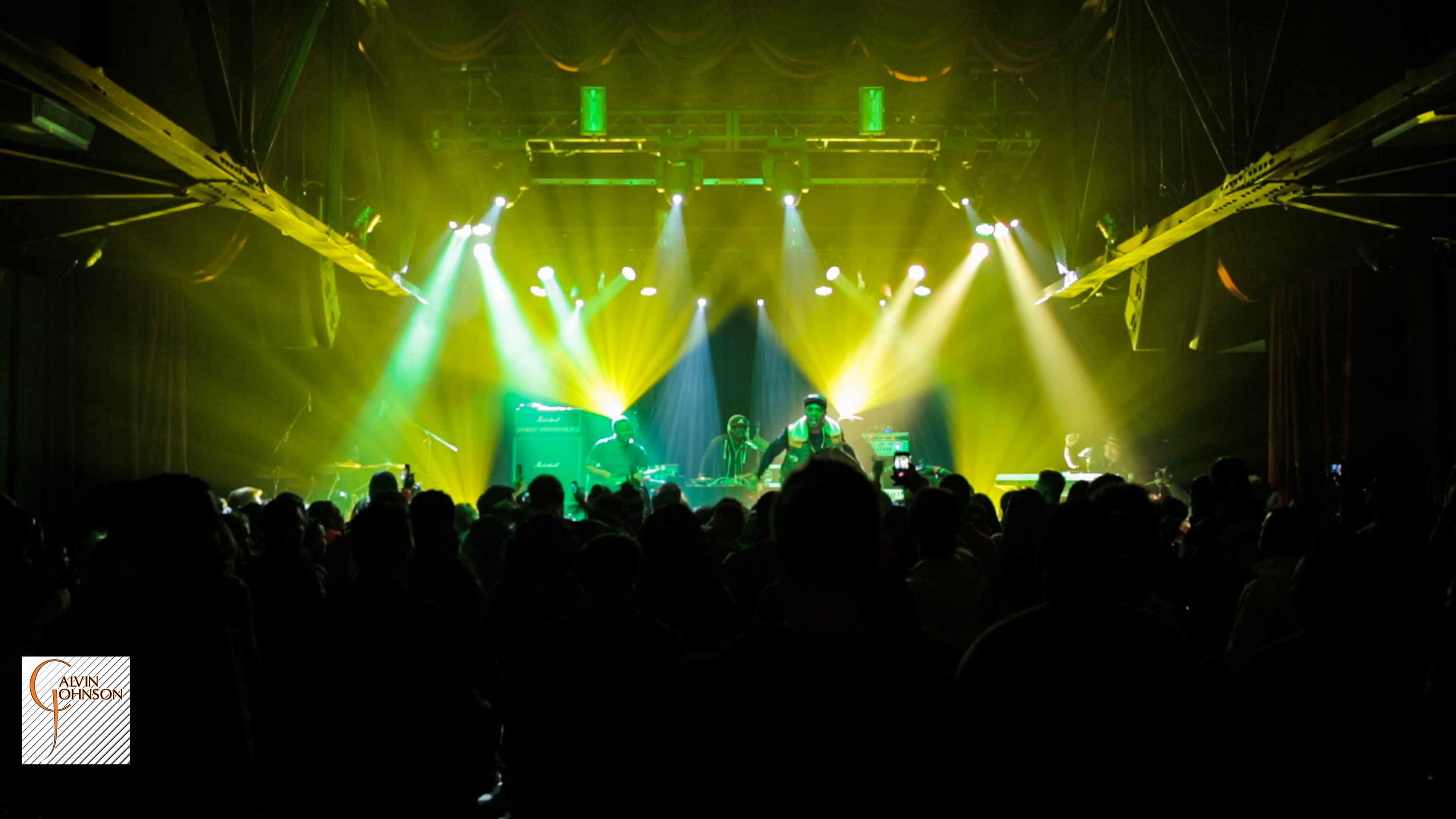 Hip Hop artist B.o.B performing in front of purple and green beams of light at a concert with DJ Shawty Slim.