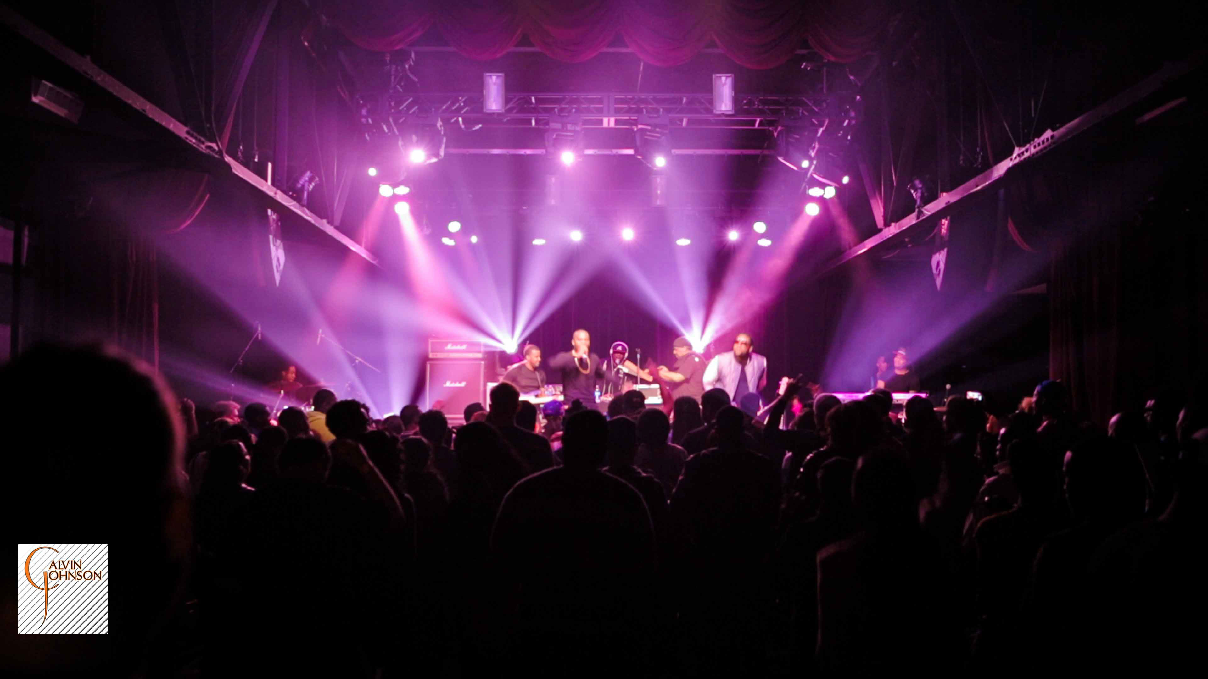 Hip Hop artist B.o.B performing in front of purple and green beams of light at a concert with DJ Shawty Slim.